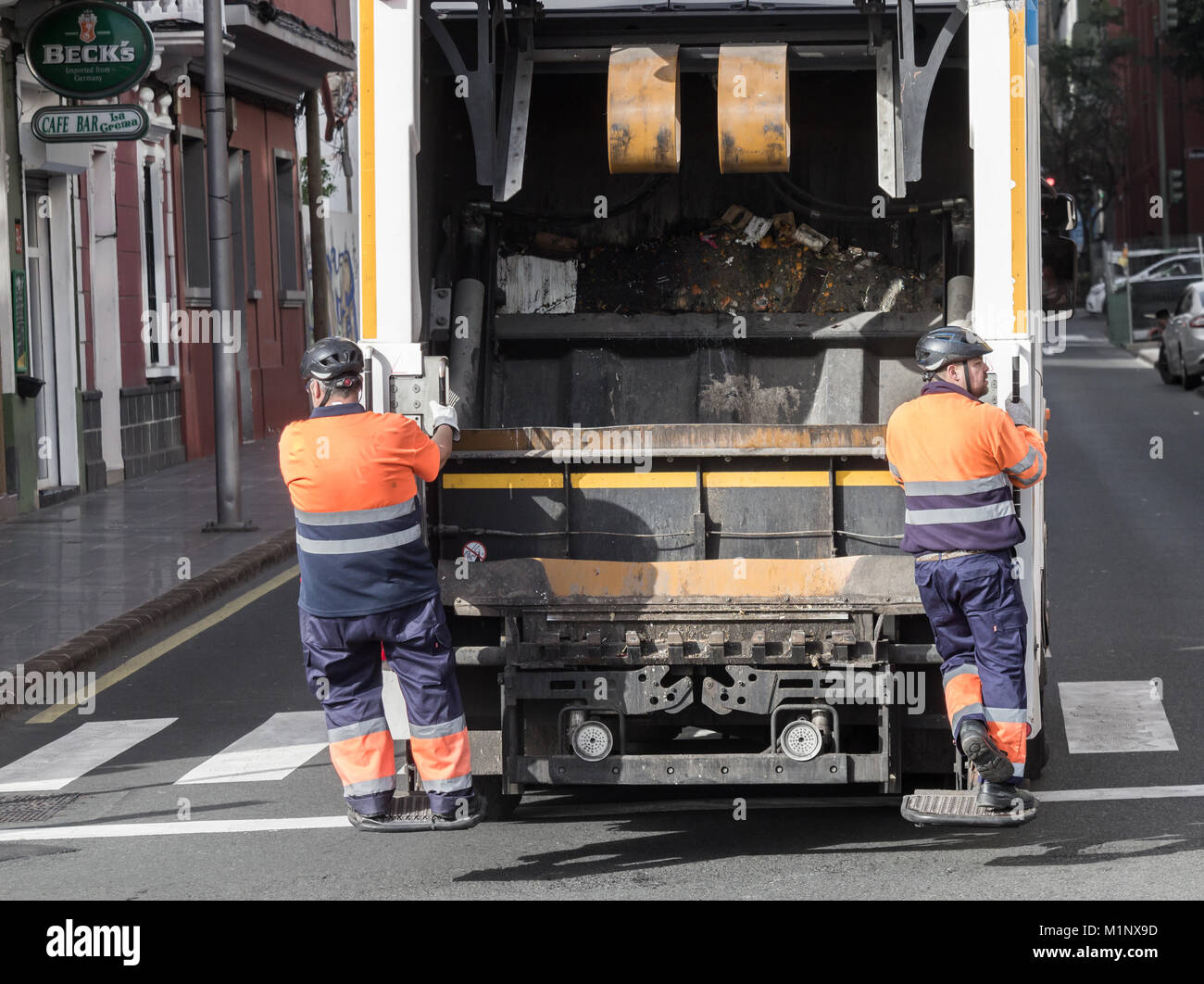 Refuse collectors riding on rear of collection lorry in Spain Stock Photo