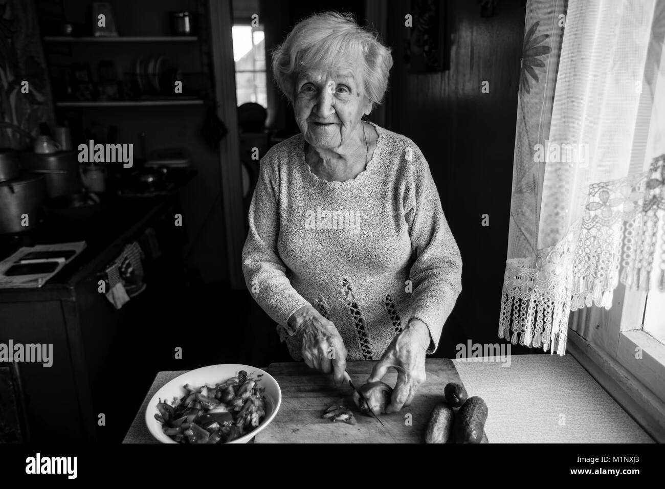 Elderly woman preparing vegetables for a salad. Black-and-white photo. Stock Photo