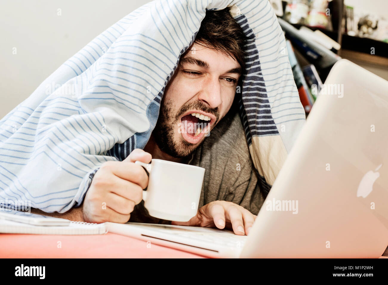 Young man learns,yawns while working at the computer in bed,home office,Germany Stock Photo