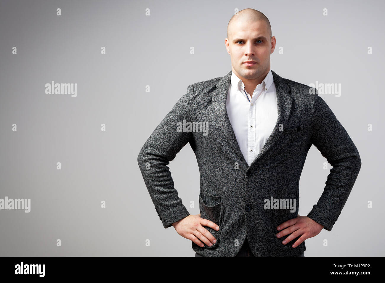 A young bald man in a white shirt, gray suit confidently looks at the camera and holds his hands on his jacket on a white isolated background Stock Photo