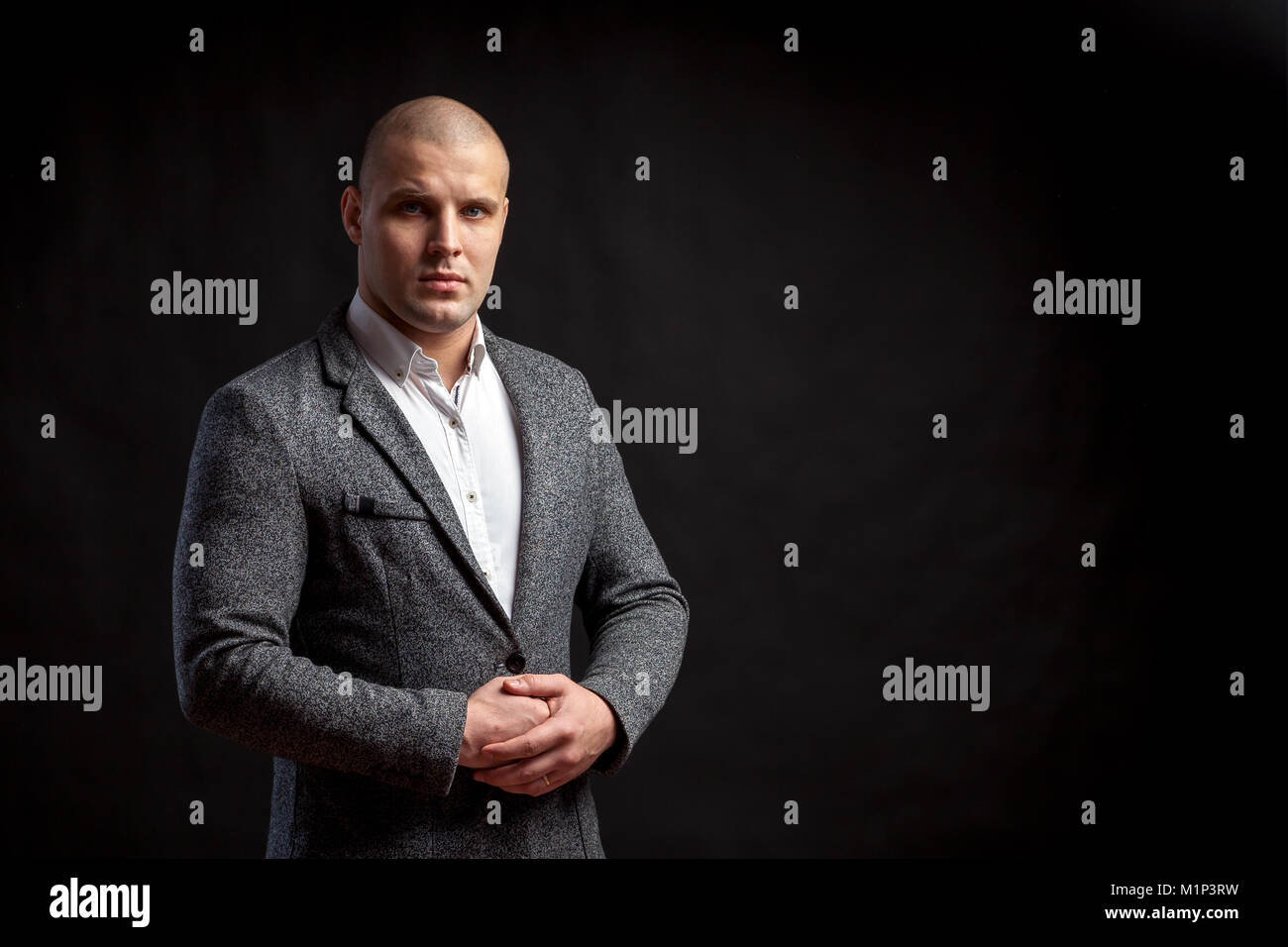 A young bald man in a white shirt, gray suit confidently looks at the camera and posing on a black isolated background Stock Photo