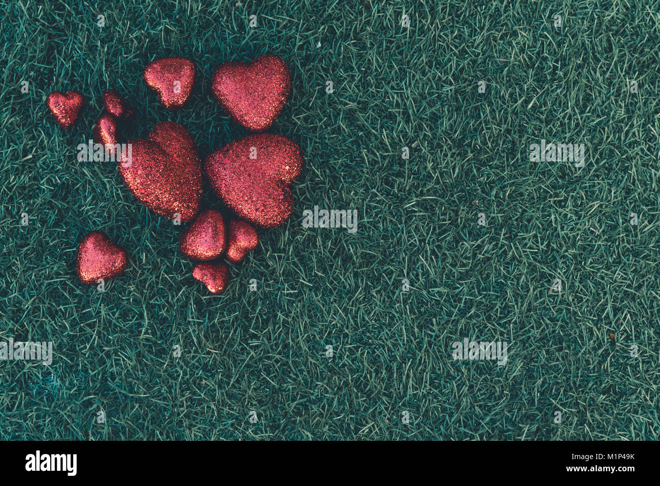 Multiple red hearts bunch up together on top of green grass leaving space on the right for text and messages Stock Photo