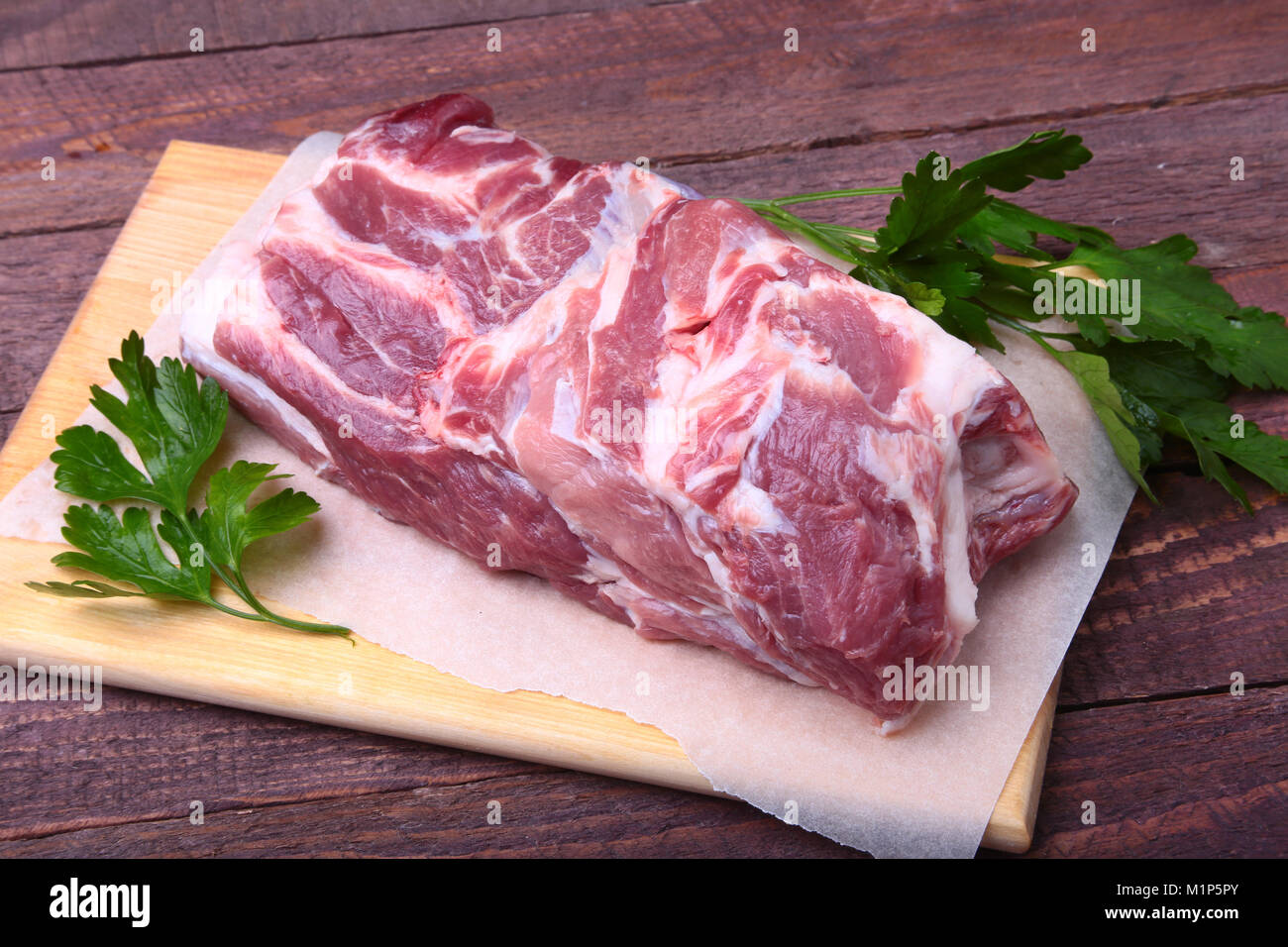 Raw pork neck chop meat with parsley herb leaves on a stone background