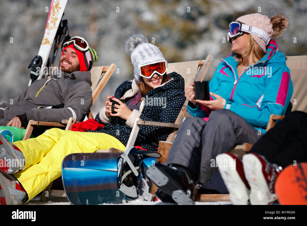 female friends enjoying hot drink in cafe at ski resort together. Sunbathing in snow Stock Photo