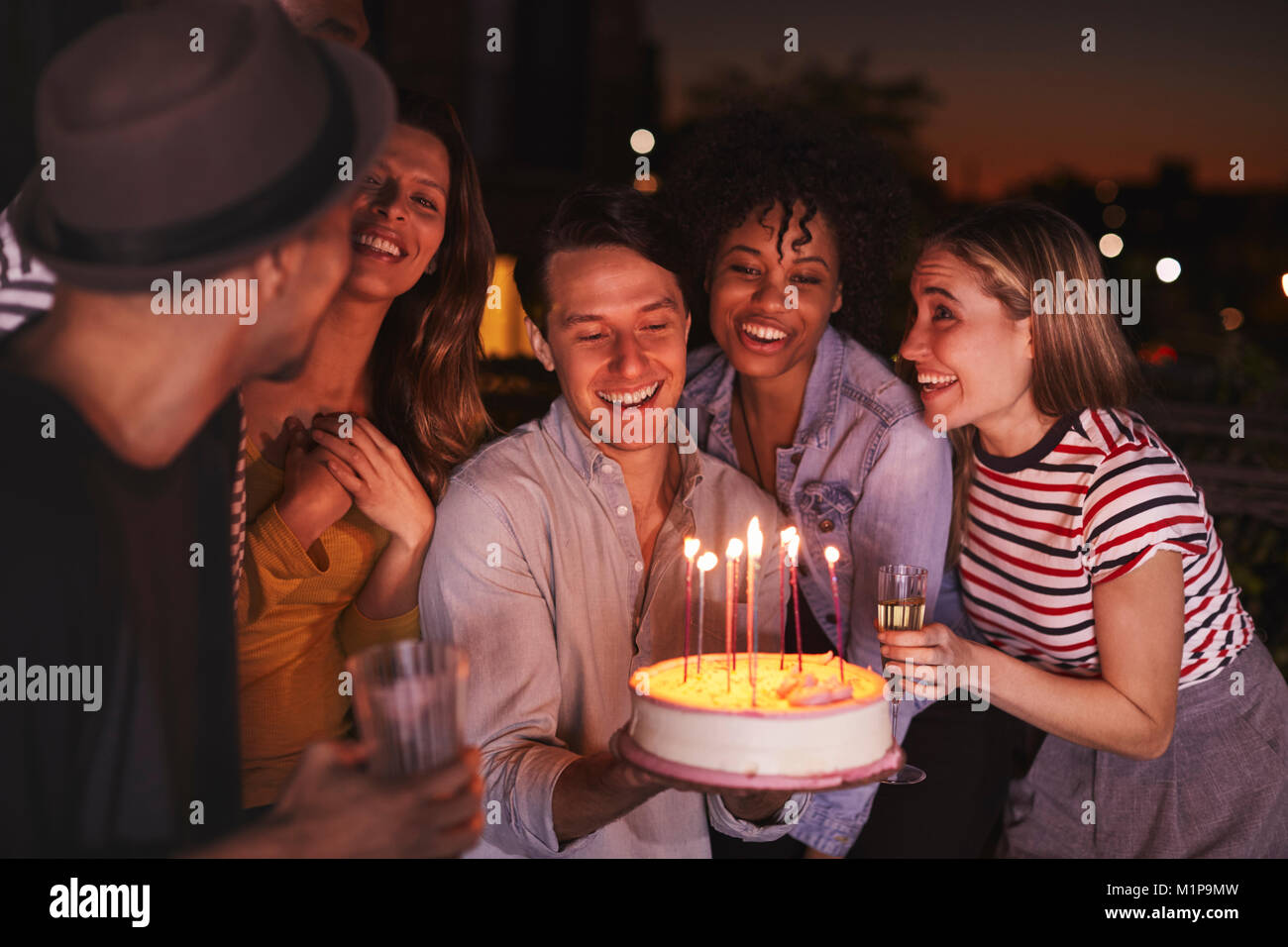 Young adults celebrating with a birthday cake on a rooftop Stock Photo