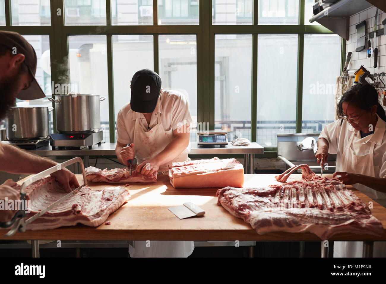 Three butchers preparing pork at a butcher's shop Stock Photo