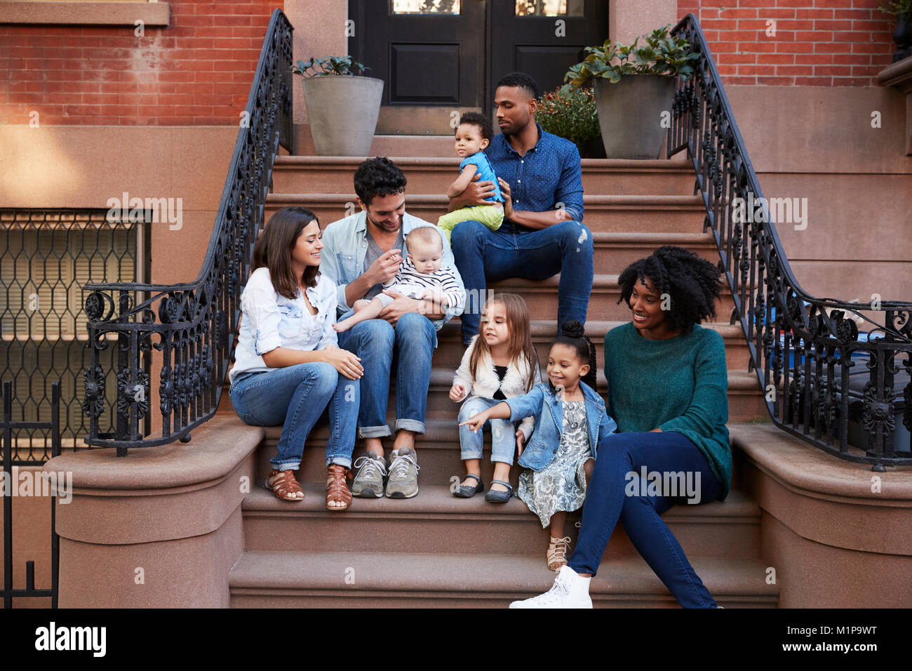 Two families with kids sitting on front stoops Stock Photo