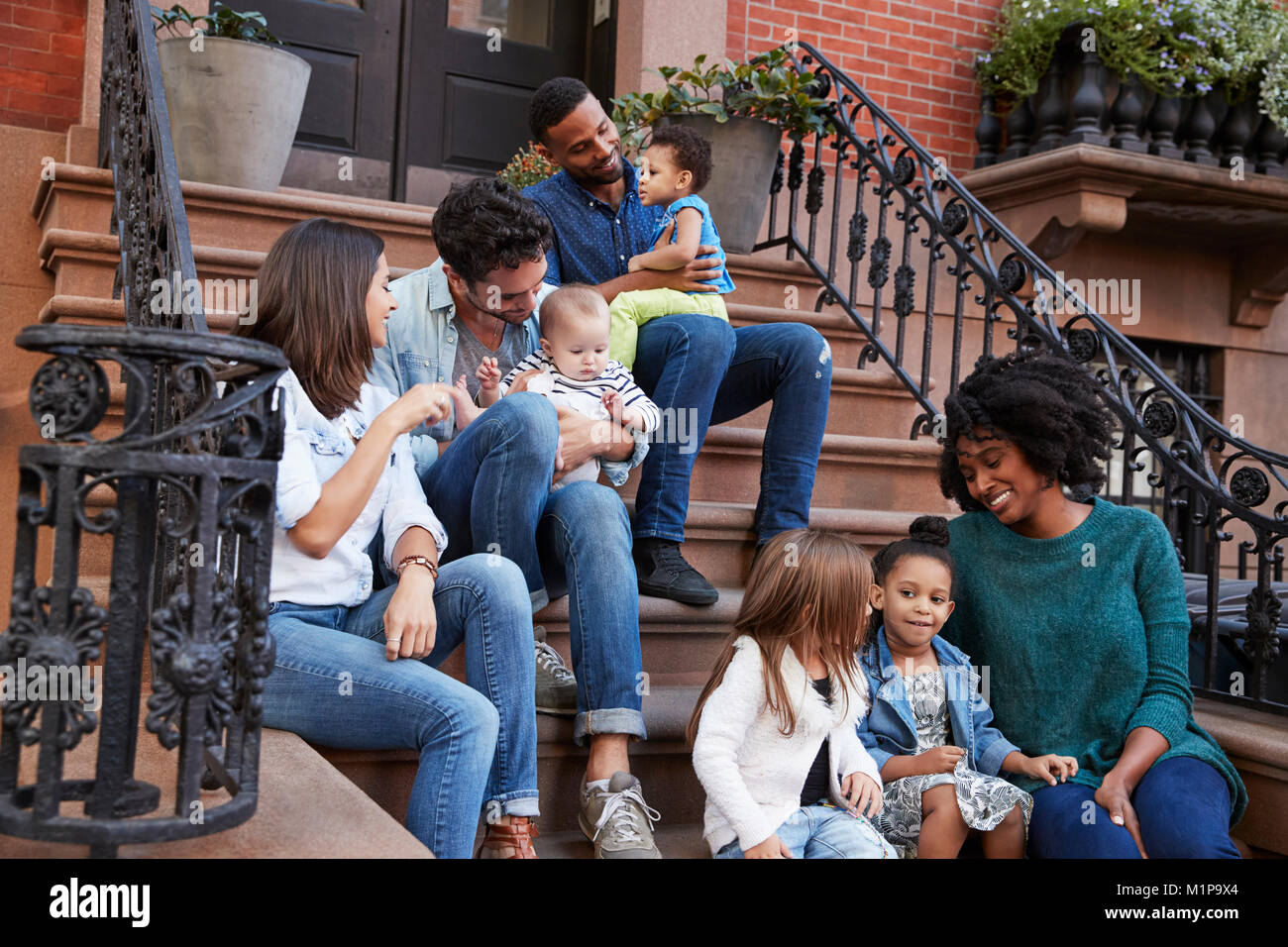 Two families with kids sitting on front stoops Stock Photo