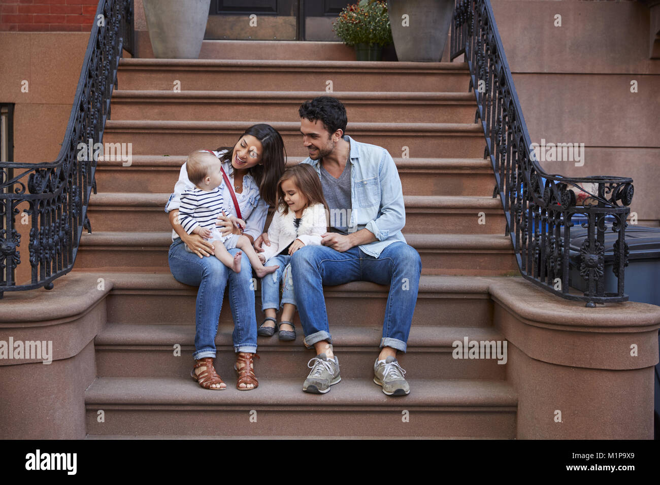 Young family with kids sitting on front stoops Stock Photo