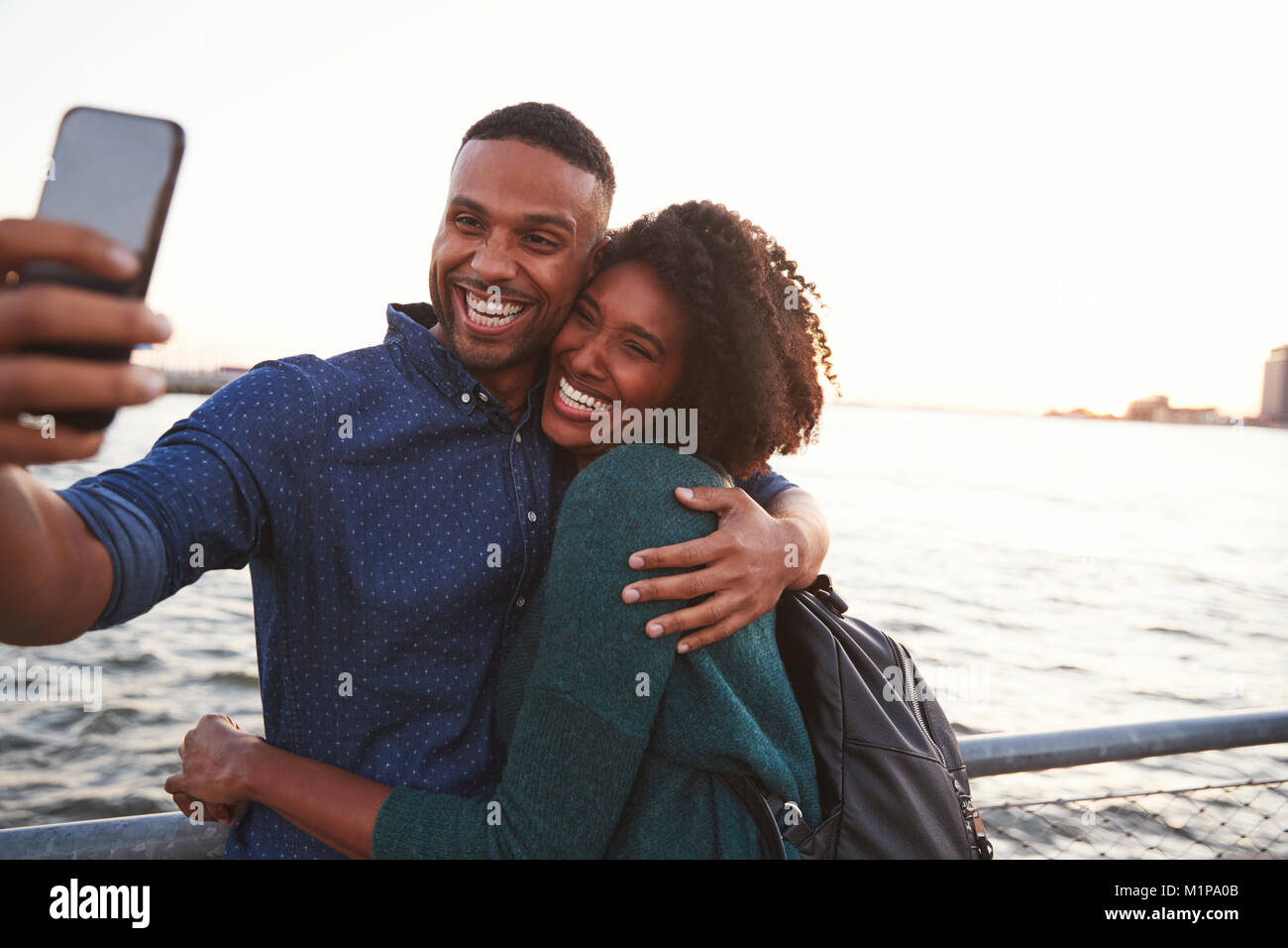 Young black couple taking photo on quayside, front view Stock Photo - Alamy