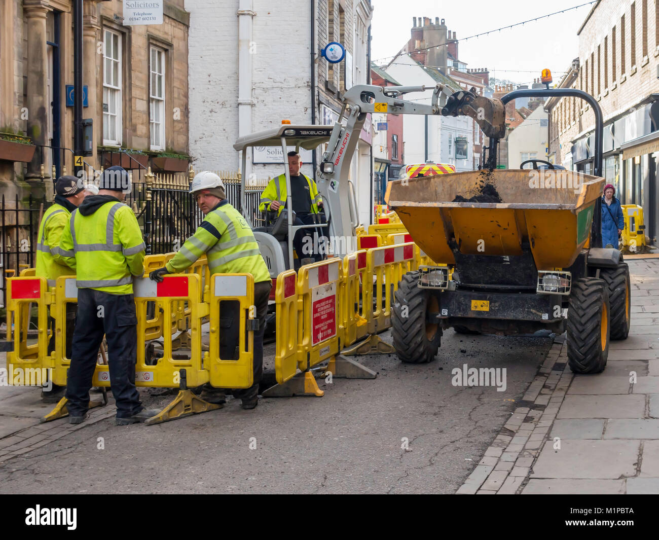 Contractors using a mini excavator to dig a trench while replacing a gas main in shopping street Baxtergate Whitby North Yorkshire England UK Stock Photo