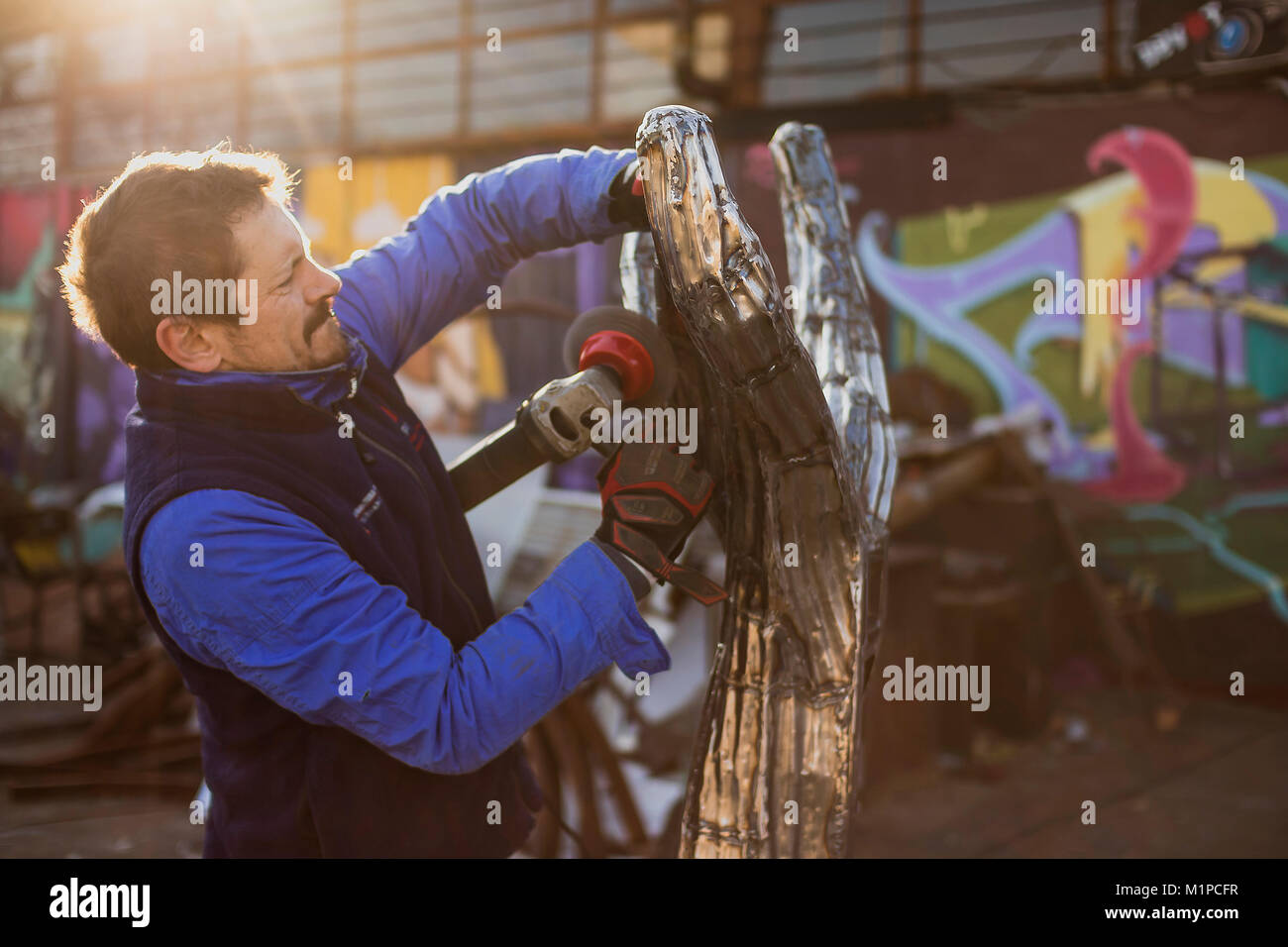 Artist grinding and Polishing his silver Tree Sculpture in the sunset outside in the front of his Work Shop but forgetting to wear his safety gear Stock Photo