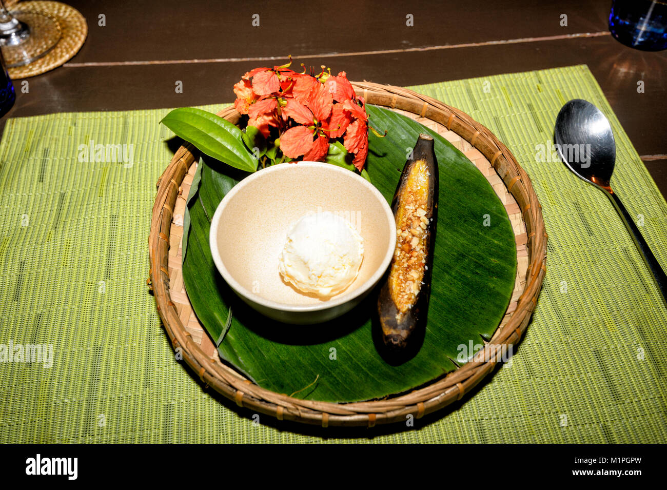 Dessert of icecream, baked banana with caramel and almonds, on a tray decorated with red hibiscus flowers, Sabah, Borneo, Malaysia Stock Photo