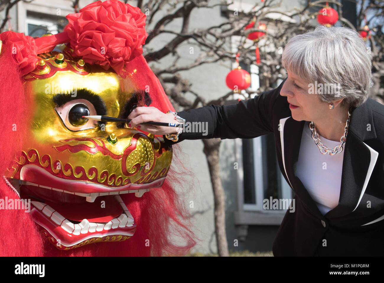 Prime Minister Theresa May 'dots the eye' of a Chinese dragon, a traditional ritual of awakening a dragon, in the grounds of the British Embassy in Beijing today on the second day of a three day trade mission to China. Stock Photo