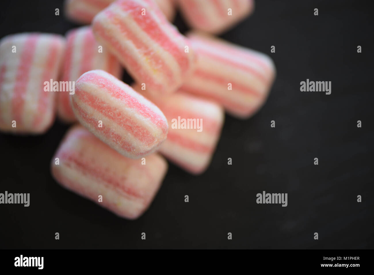 food of sugar coated sweets treats or candy in pastel colors and stripe patterns on a black slate background with space Stock Photo