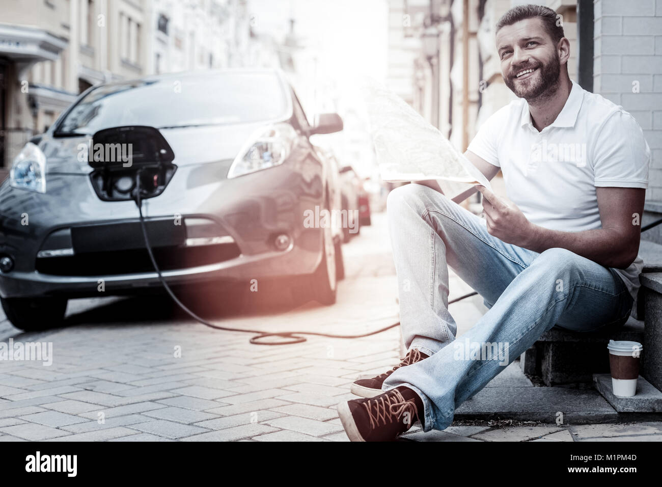 Positive minded man grinning broadly while charging his electric car Stock Photo