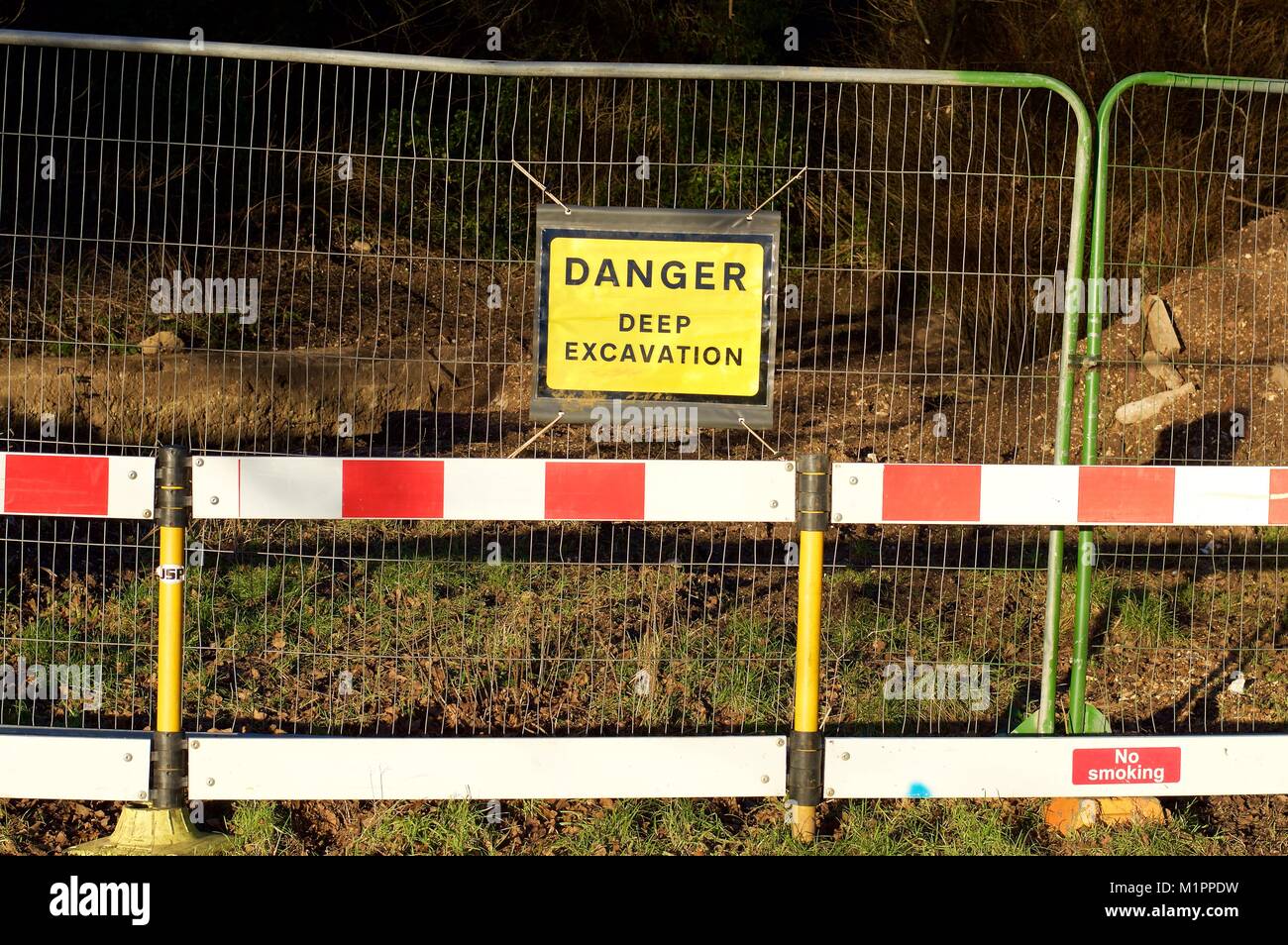 Fencing erected around a large hole during building works, with a sign reading 'Danger, deep excavation' Stock Photo