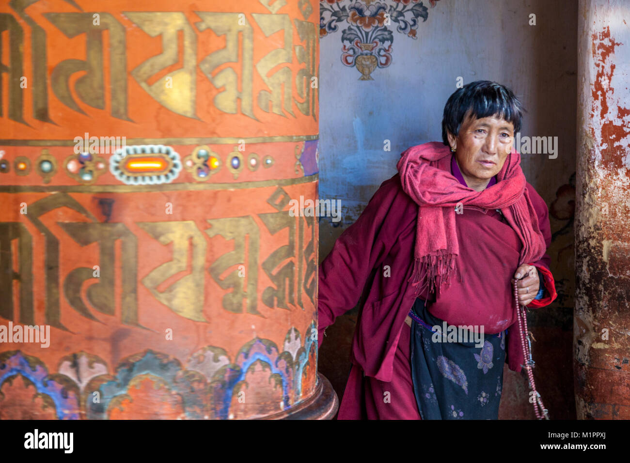 Bumthang, Bhutan.  Woman Turning Large Prayer Wheel,  Jambay Lhakhang Monastery. Stock Photo