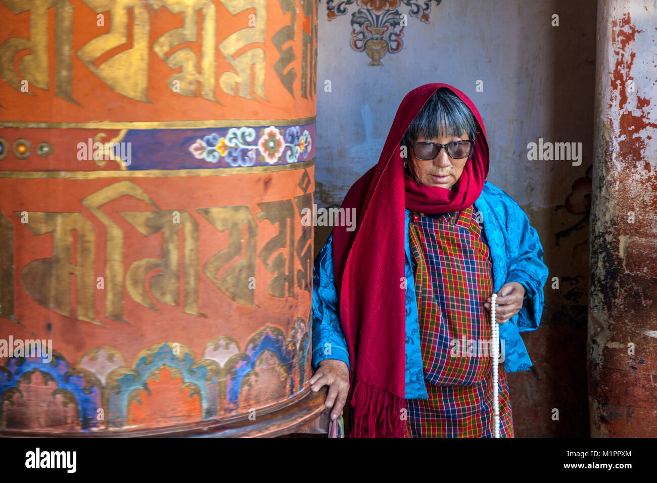 Bumthang, Bhutan.  Woman Turning Large Prayer Wheel,  Jambay Lhakhang Monastery. Stock Photo