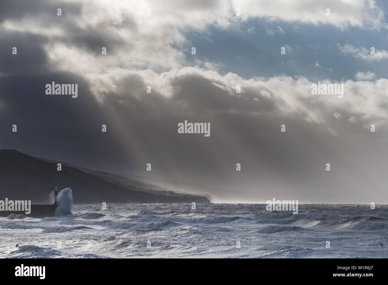 Sunbeams break through clouds as a rough sea caused by Storm Eleanor batters the Cardigan Bay coastline at Aberystwyth Stock Photo