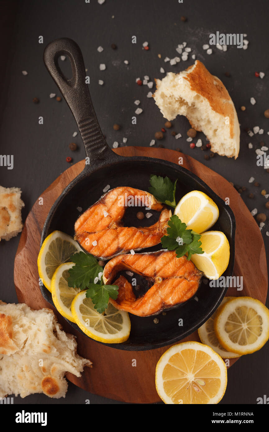 Fried or grilled salmon fillet on castiron pan with bread and lemon