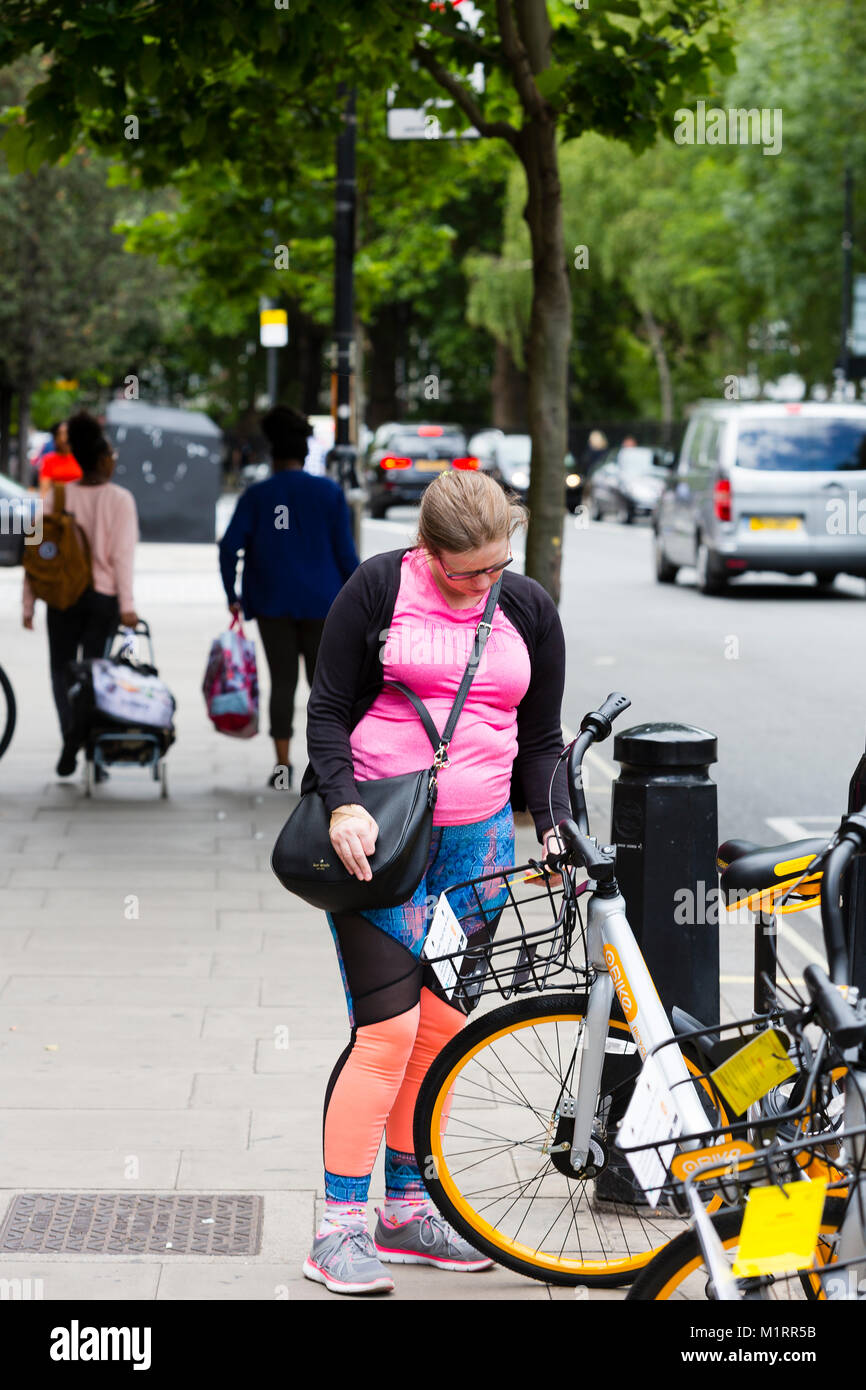 LONDON, ENGLAND. A pedestrian pauses to read an enforcement notice attached to an Obike from Hammersmith and Fulham council warning that the bikes are Stock Photo