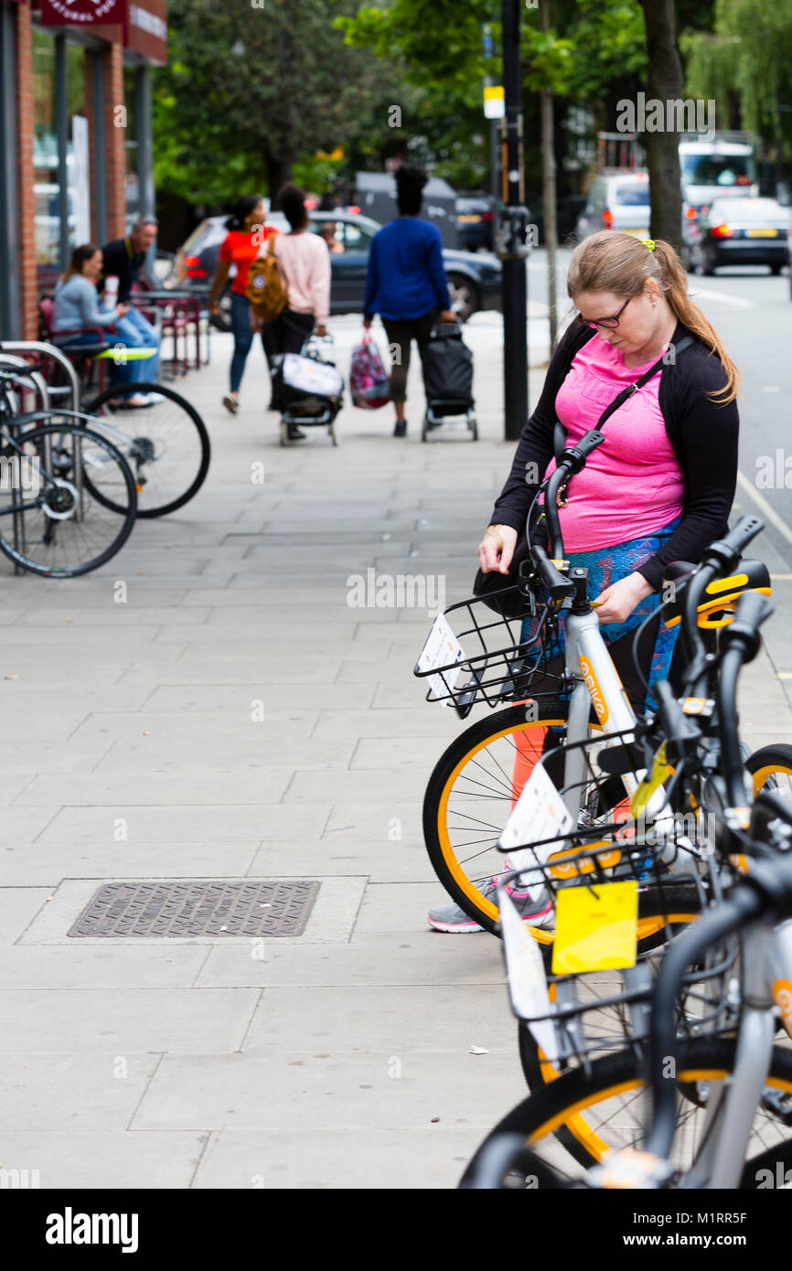 LONDON, ENGLAND. A pedestrian pauses to read an enforcement notice attached to an Obike from Hammersmith and Fulham council warning that the bikes are Stock Photo