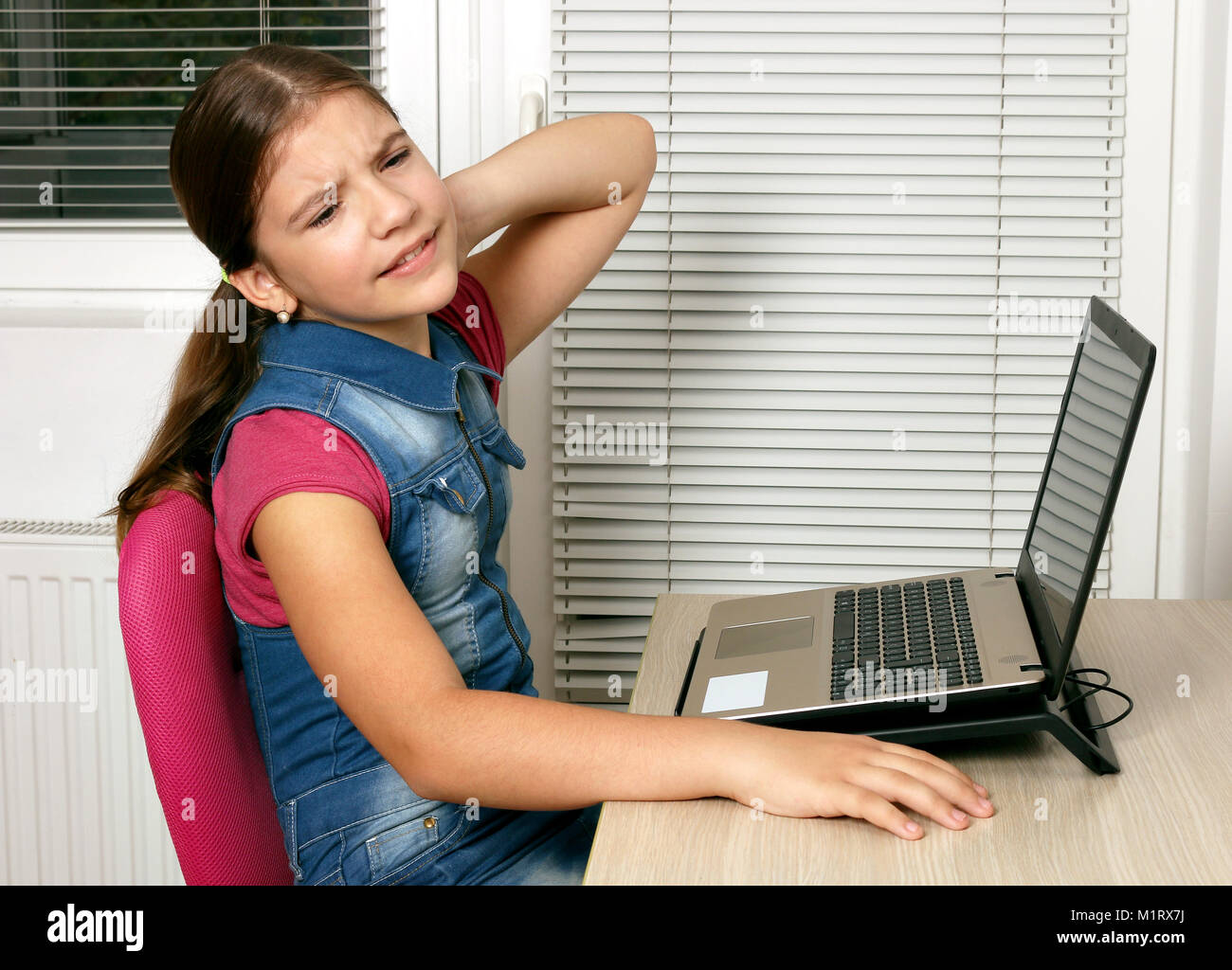 unhappy little girl has pain in her neck while using a laptop Stock Photo