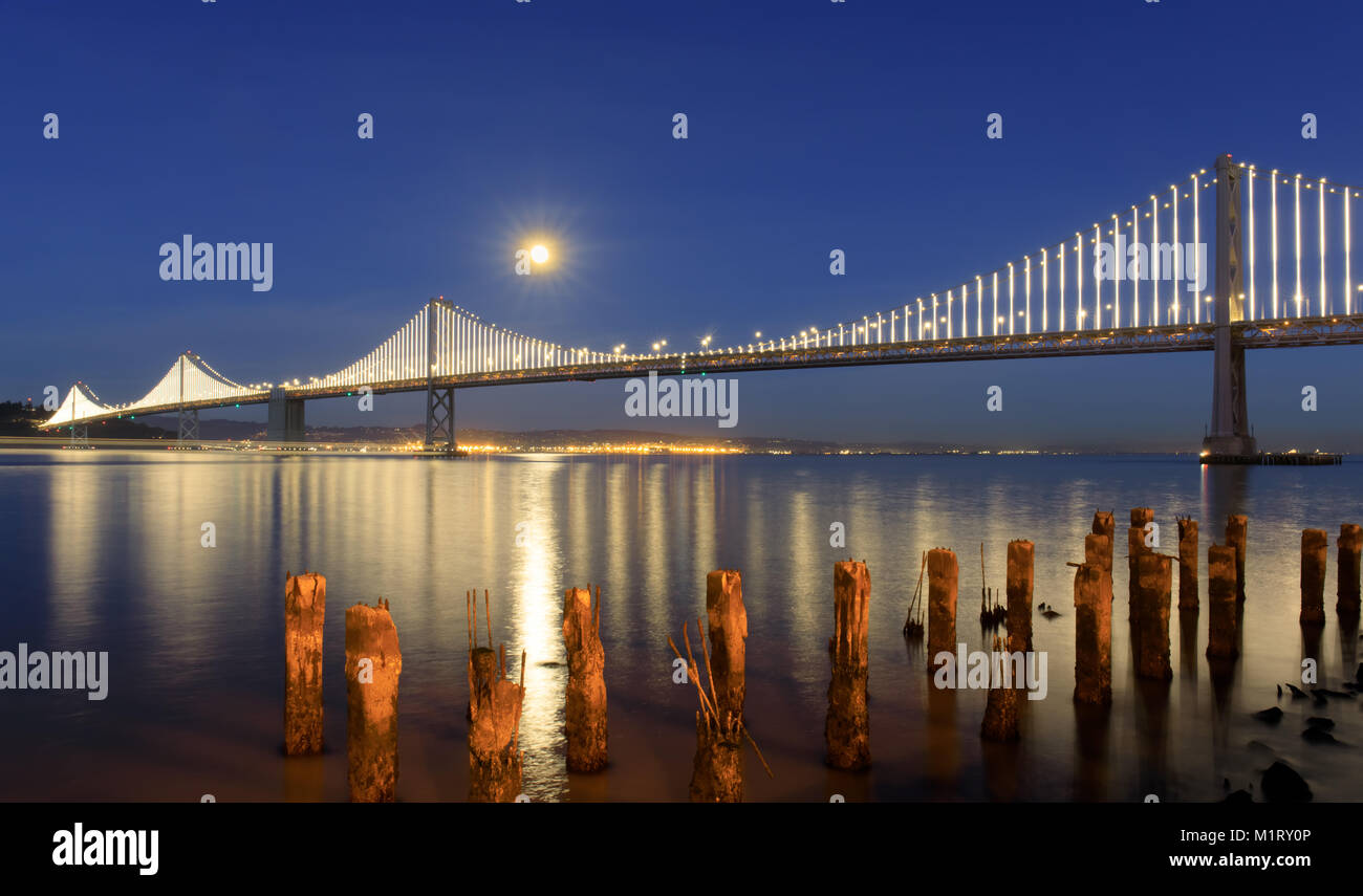 San Francisco-Oakland Bay Bridge with full moon rising at dusk. Stock Photo