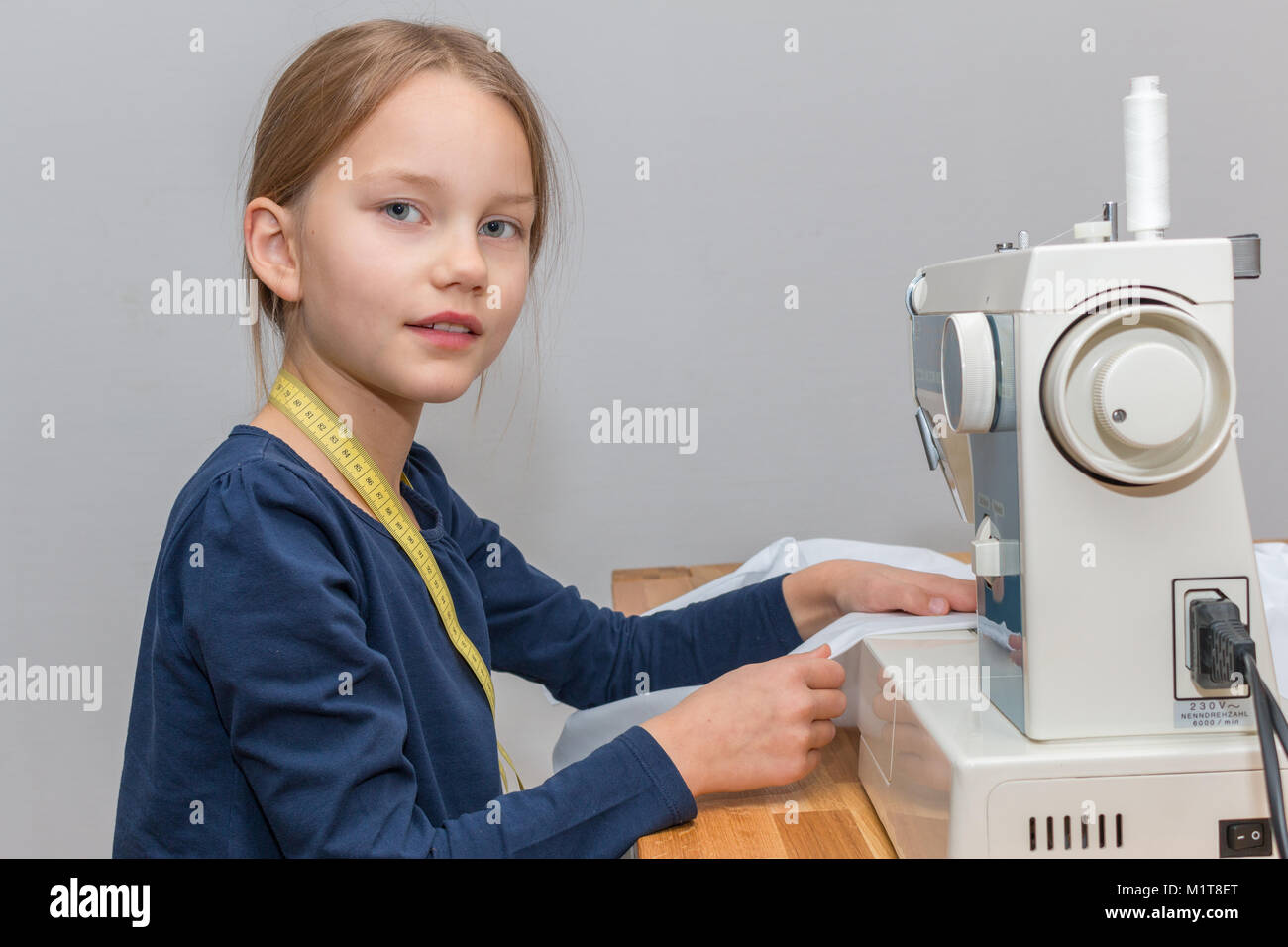 Portrait of a 8 year old girl sewing a pink and white striped cloth with a sewing machine, smiling Stock Photo