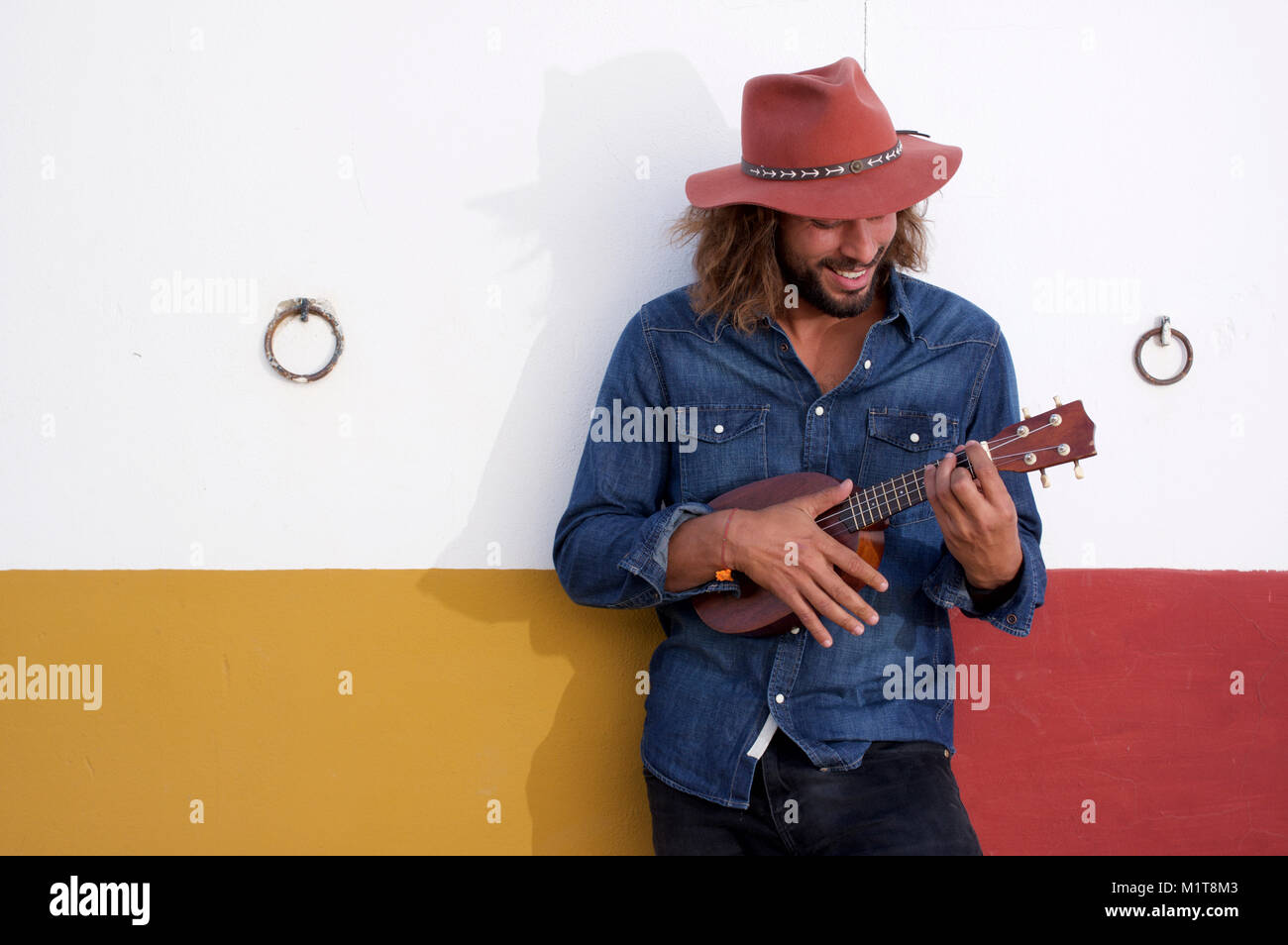 Man in red hat strumming a ukulele Stock Photo