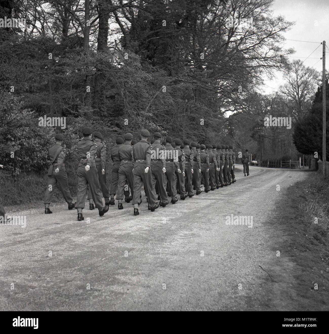 1955, historical, Bucks, England, a troop of British soldiers on a training drill outdoors, the servicemen are marching on a gravel track through a wooded area. Stock Photo