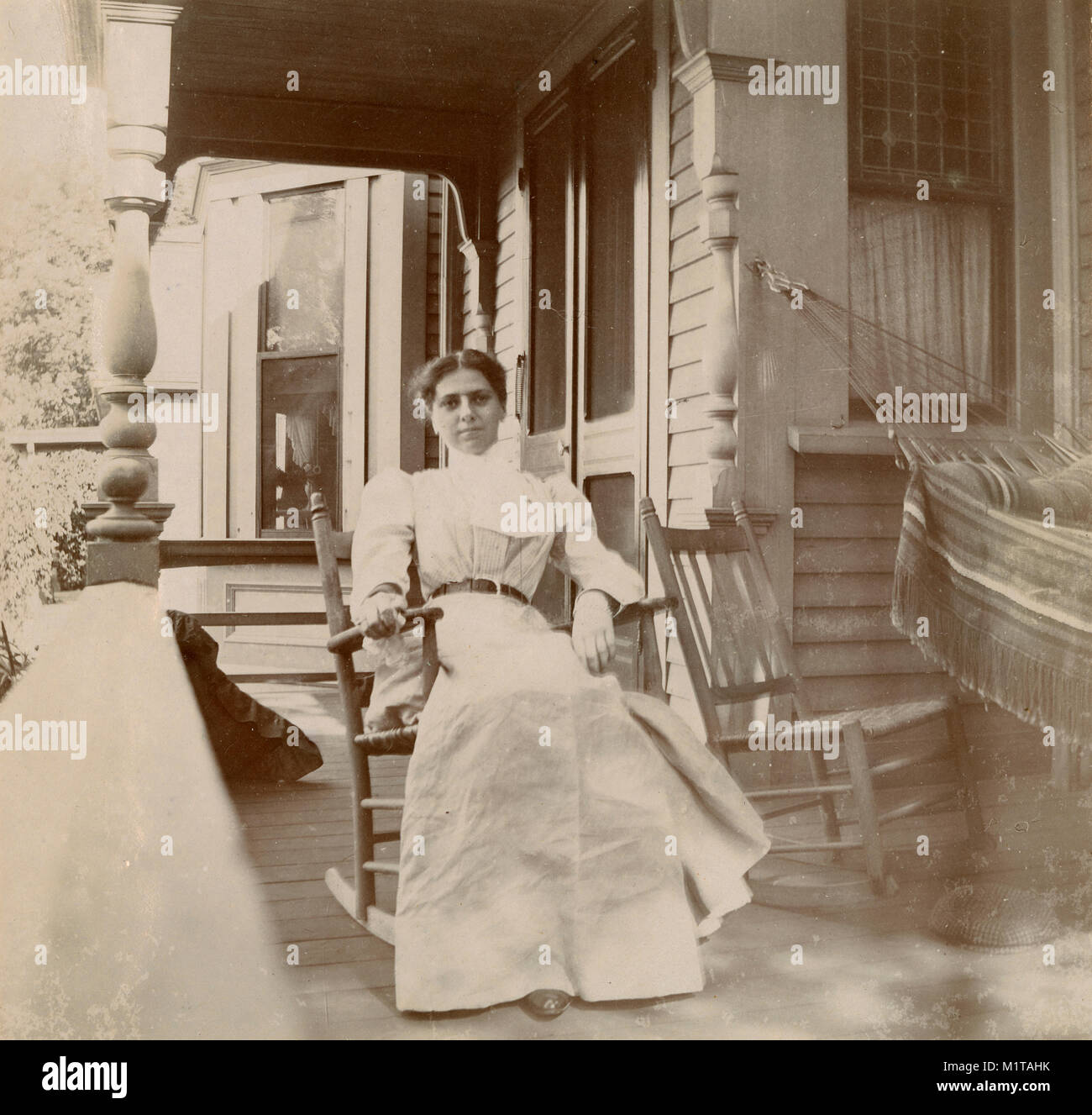 Antique circa 1905 photograph, woman in a rocking chair on her porch. Location unknown, probably New England, USA. I have more photos of this family in Riggsville (now Robinhood), Maine in Sagadahoc County, USA. Stock Photo
