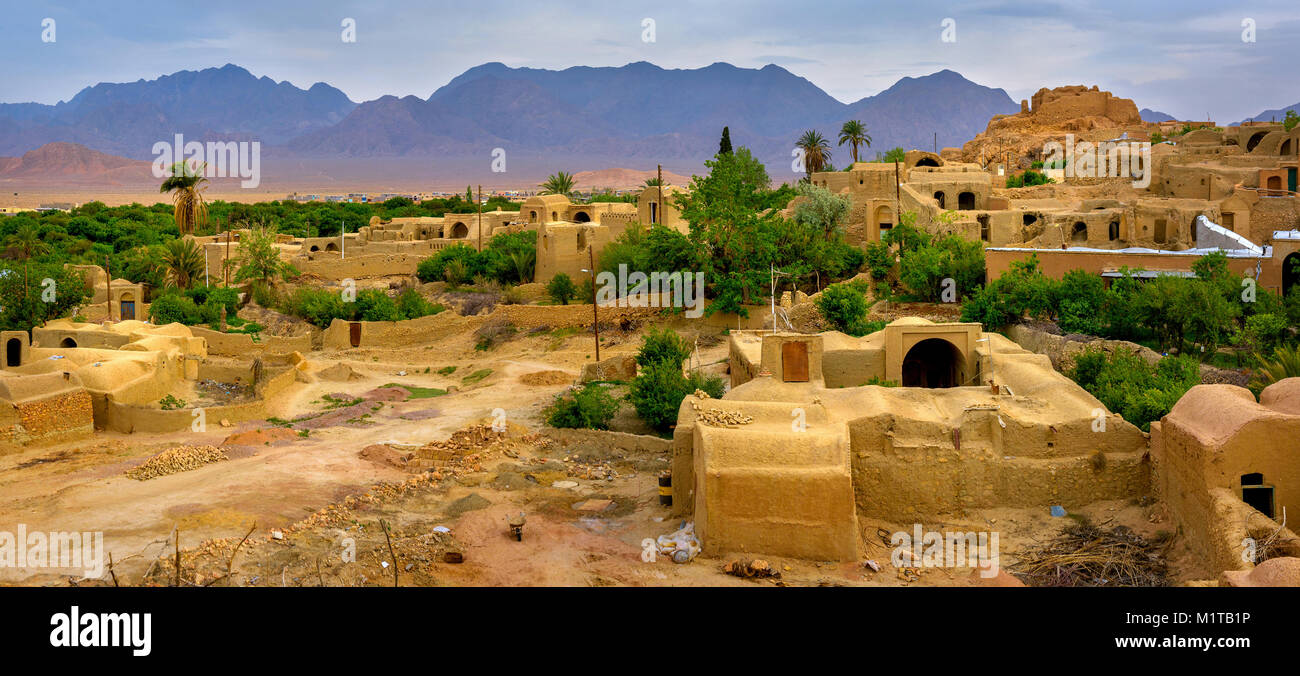 The village of clay houses in an oasis in the middle of the desert in Iran, on a background mountains tower Stock Photo