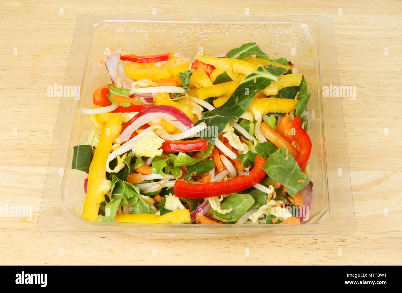 Stir fry vegetables in a plastic carton on a wooden chopping board Stock Photo