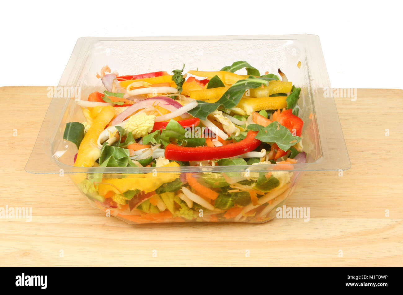 Stir fry vegetables in a plastic carton on a wooden chopping board against a white background Stock Photo