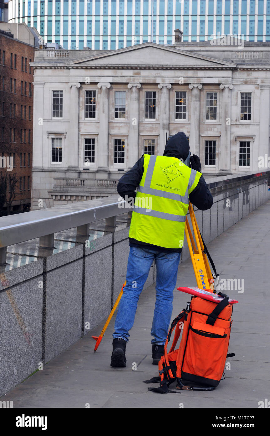 a construction worker or engineer measuring buildings and structures using a theodolite on a yellow tripod. A surveyor working in High visibility vest Stock Photo