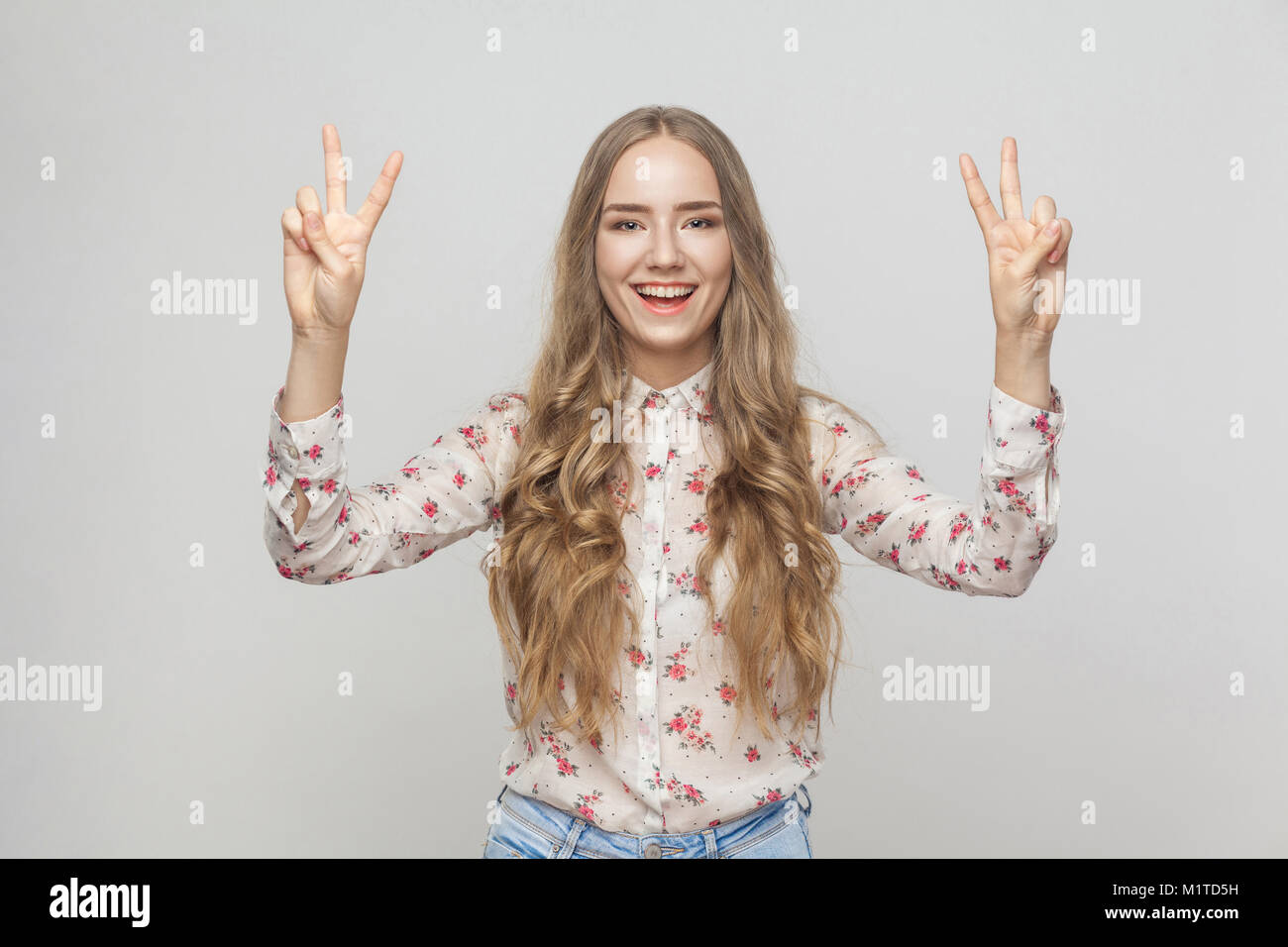 Young adult woman showing peace sign and toothy smiling. Studio shot Stock Photo
