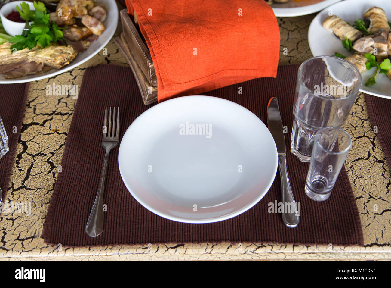 on the brown napkin, on the table is flatware per person, fork, knife, two glasses, on the background there are rolls of eggplant and grilled vegetabl Stock Photo