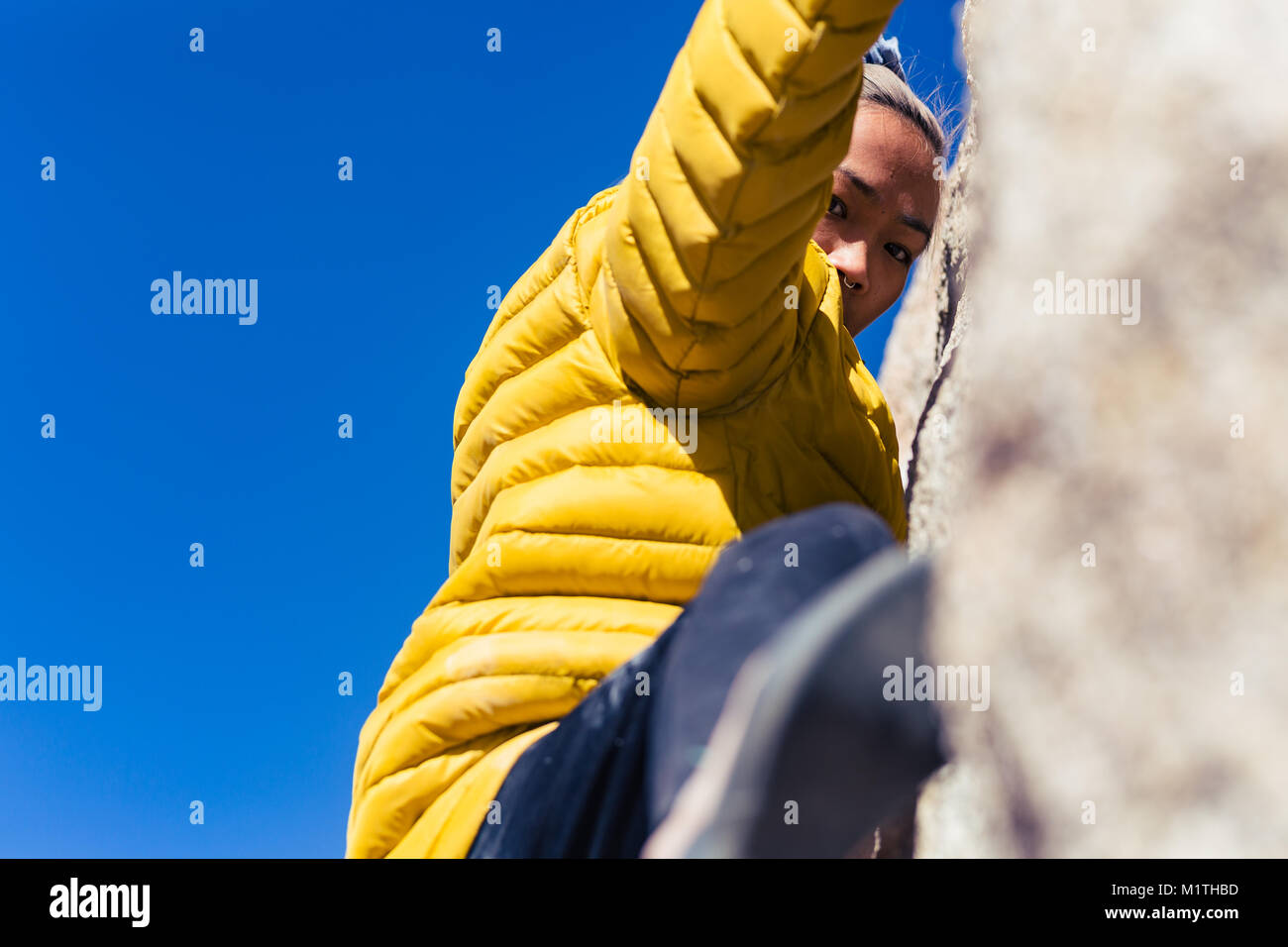Petite asian woman rock climbing outdoors hangs from stone wall while