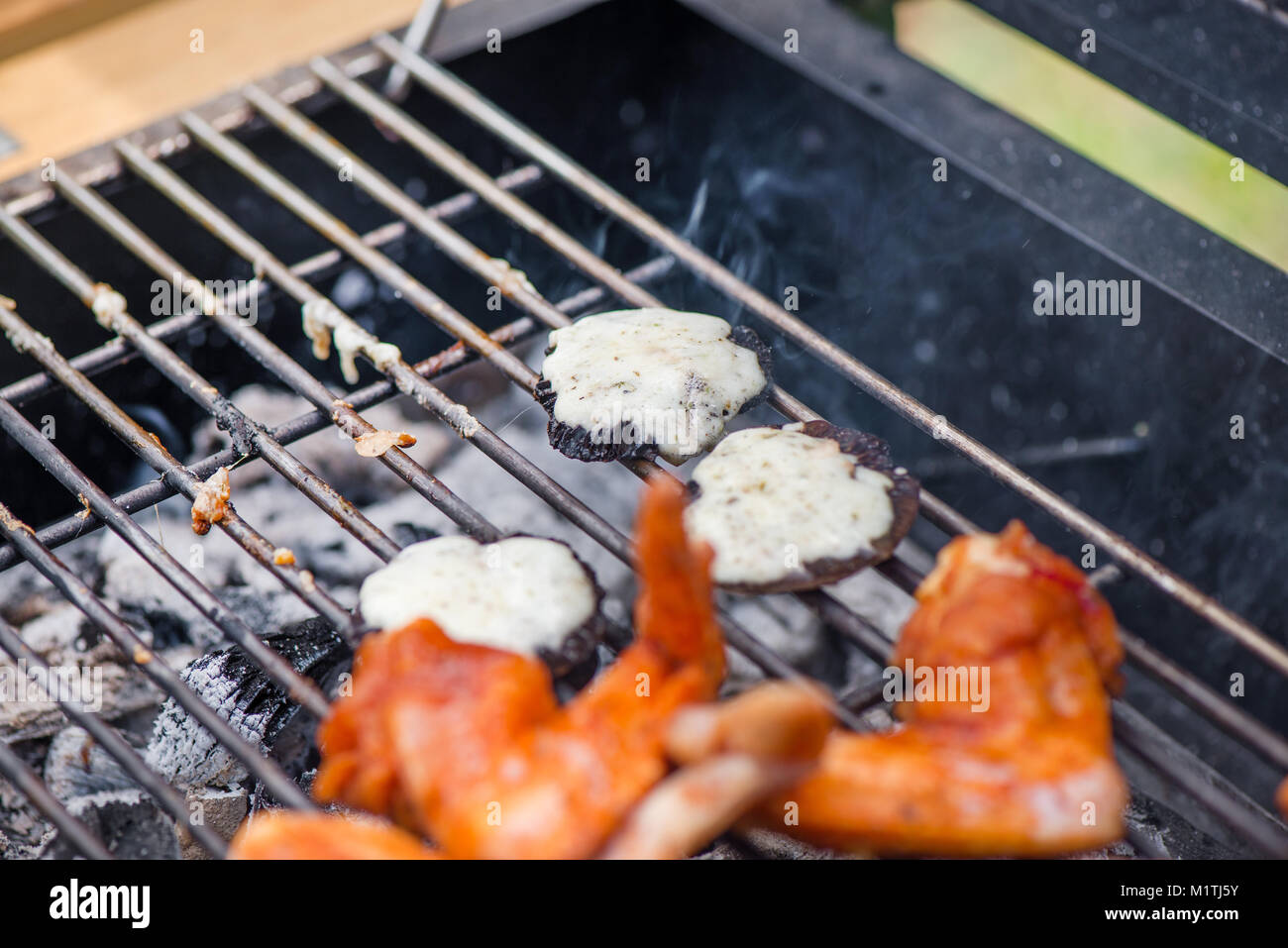 Mushrooms with cheese and chicken wings on barbecue grill on hot