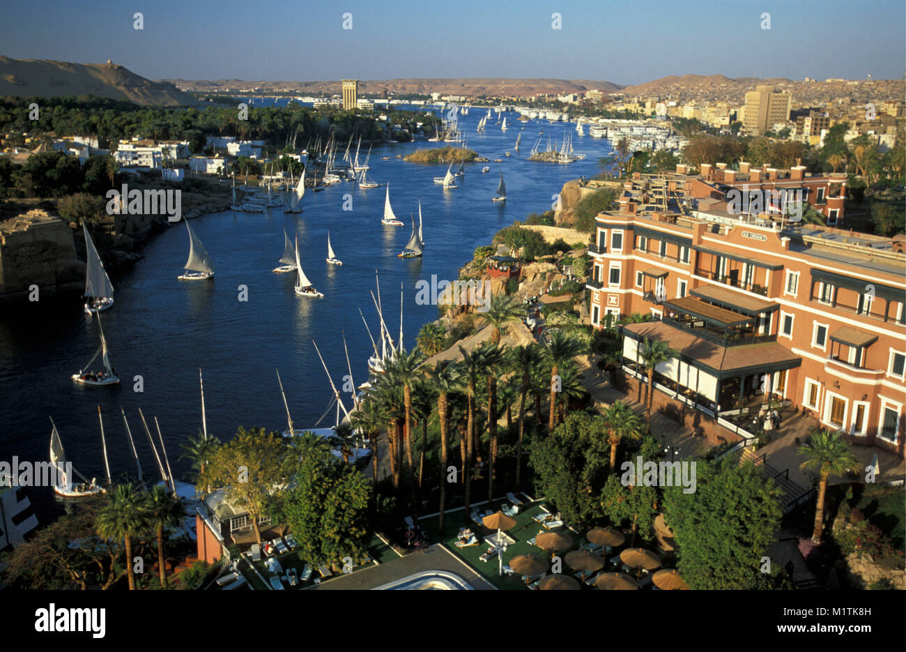Egypt. Aswan. Nile river. Feluccas (traditional sailing ships). In front: The Old Cataract Hotel, famous and historic hotel. Stock Photo