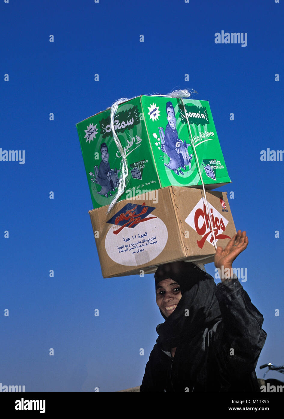 Egypt, Luxor. East Bank. Woman carrying boxes from market on head. Stock Photo