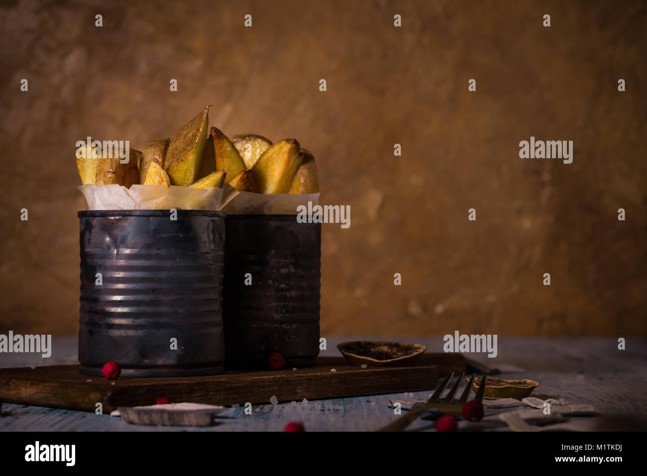 Horizontal photo with two vintage cans with worn surface full of roasted potato strips. Potatoes are un-peeled and fried with skin. Cans are on vintag Stock Photo