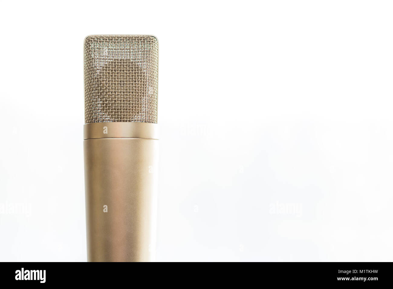An old fashioned gold microphone is placed upright on a stand.  The background is all white. There is plenty of copy space. Stock Photo
