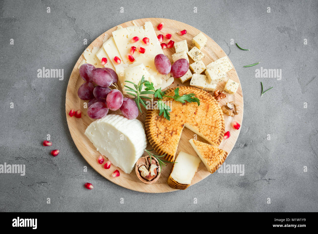 Cheese platter with assorted cheeses, grapes, nuts over gray stone