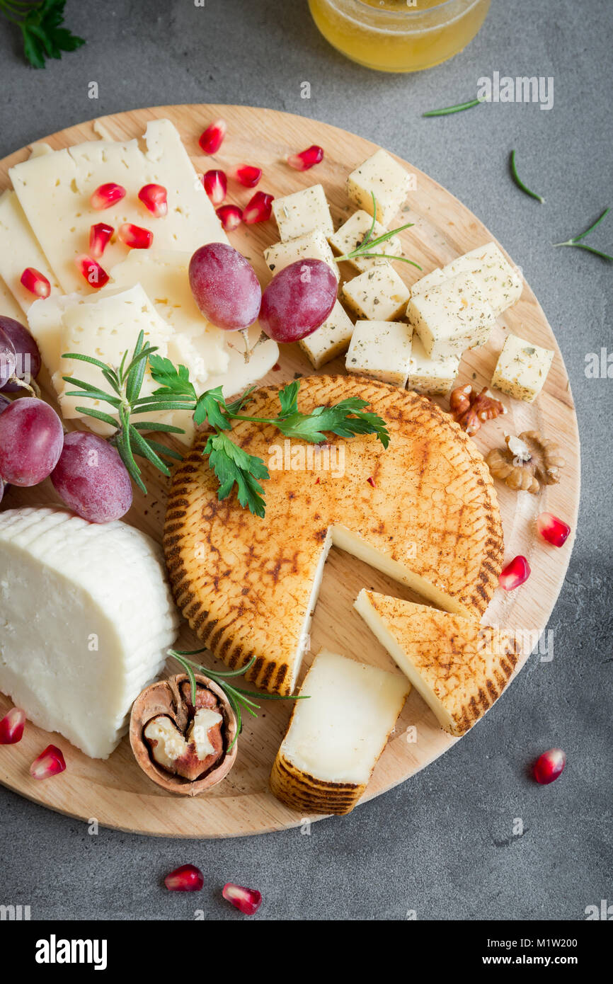 Cheese platter with assorted cheeses, grapes, nuts over gray stone