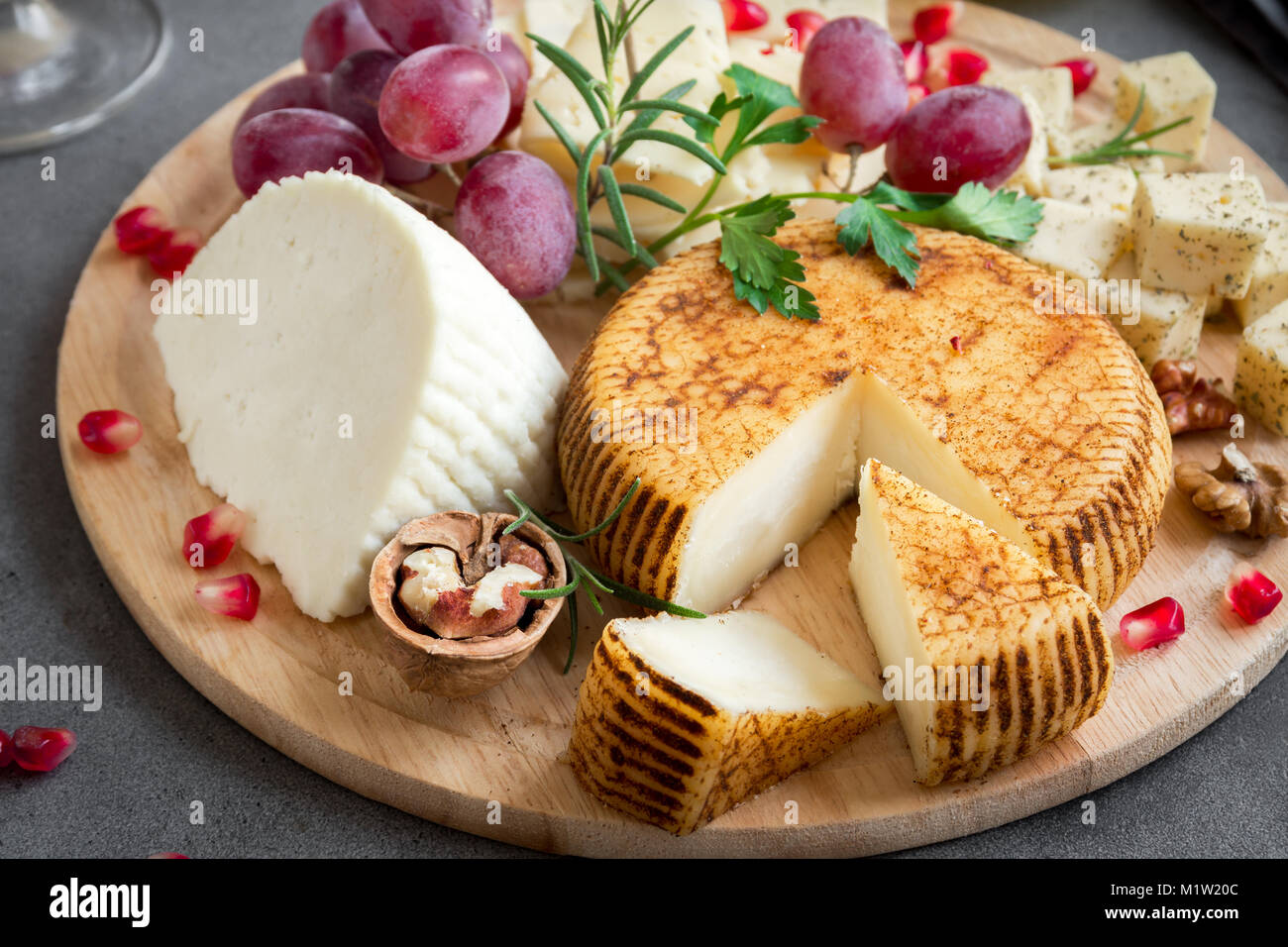 Cheese platter with assorted cheeses, grapes, nuts over gray stone