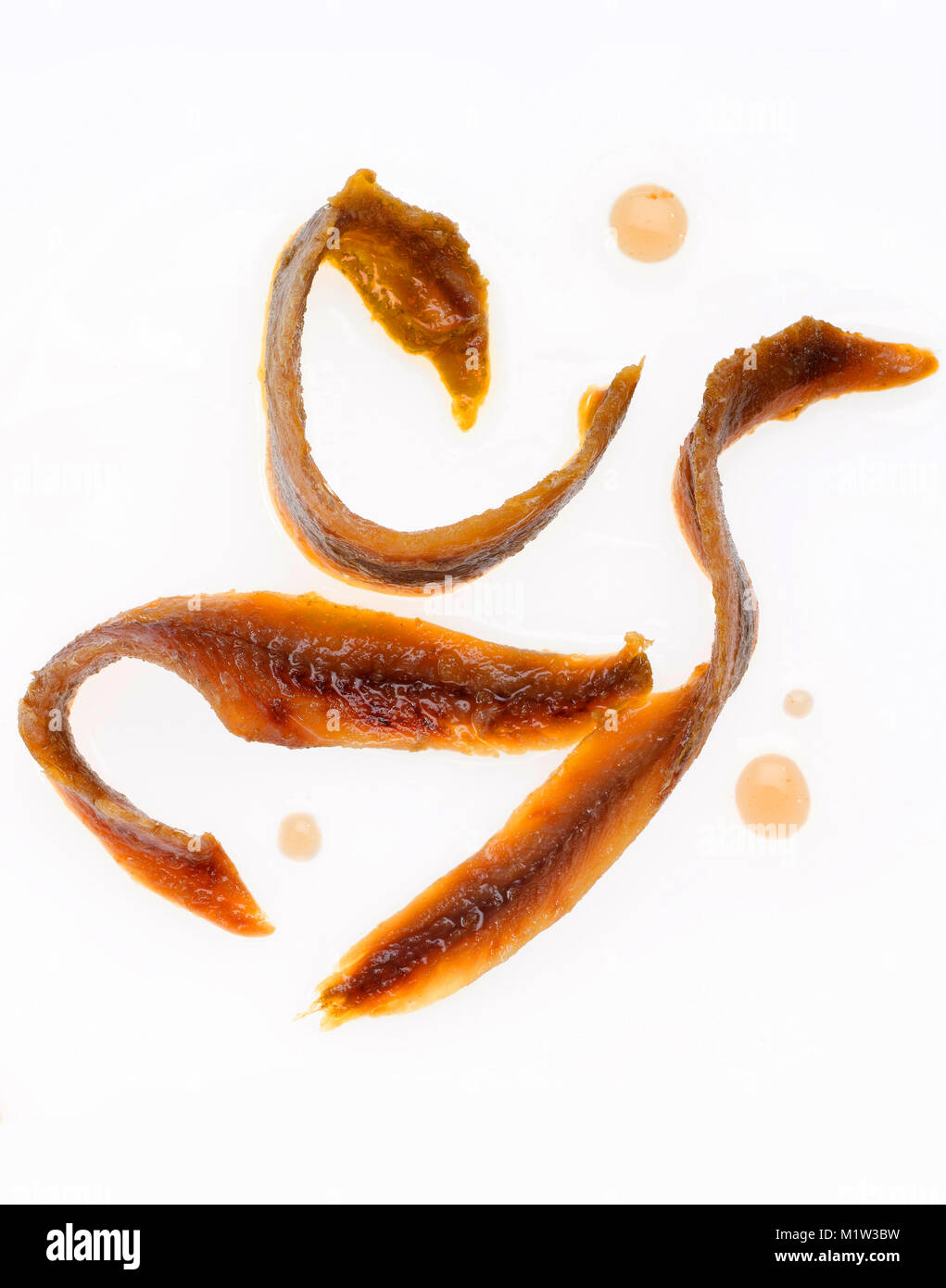 High Angle View of Three Anchovy Fillets with Drops of Oil Against White Background Stock Photo