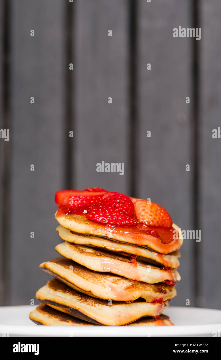 Delicious Strawberry Pancakes on a dark moody background, stunning breakfast with vibrant colors, white plate Stock Photo